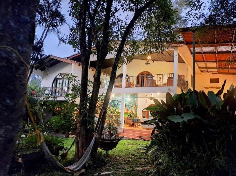 Villa Chelsey at dusk — lit terraces and balconies seen from the garden, with a hammock between the trees